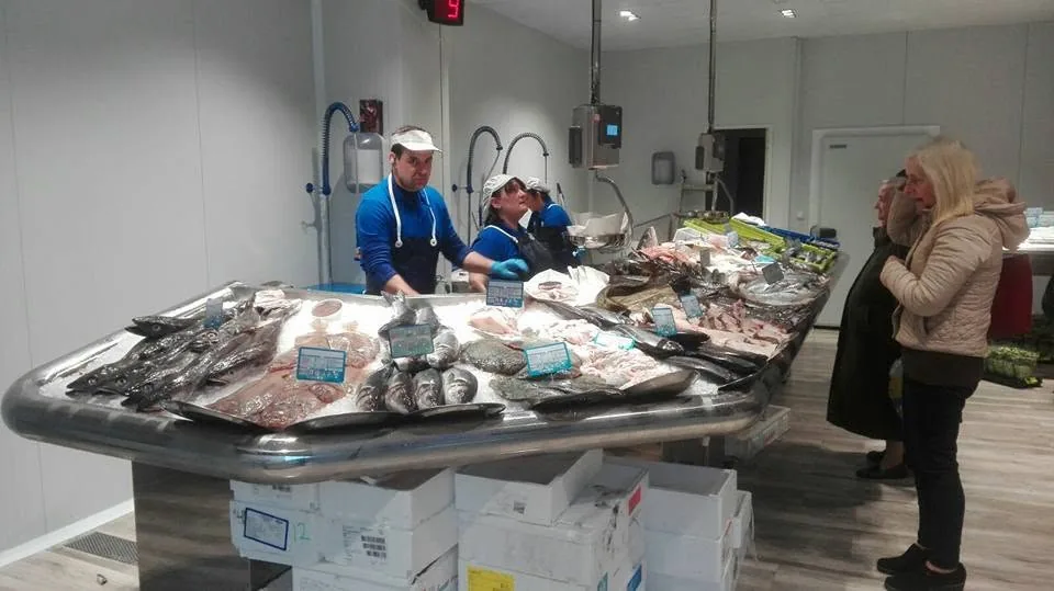 Mostrador de pescado fresco con personal y una clienta en la zona de venta