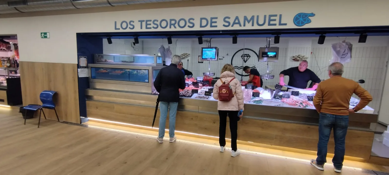 Vista de una pescadería con mostrador de producto fresco, vivero y personas en la zona de venta